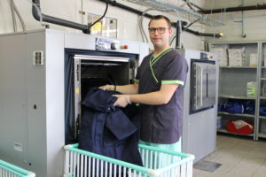 Un jeune homme en situation de handicap sort du linge de la machine à laver professionnelle de la blanchisserie de l'ESAT de la Ballastière
